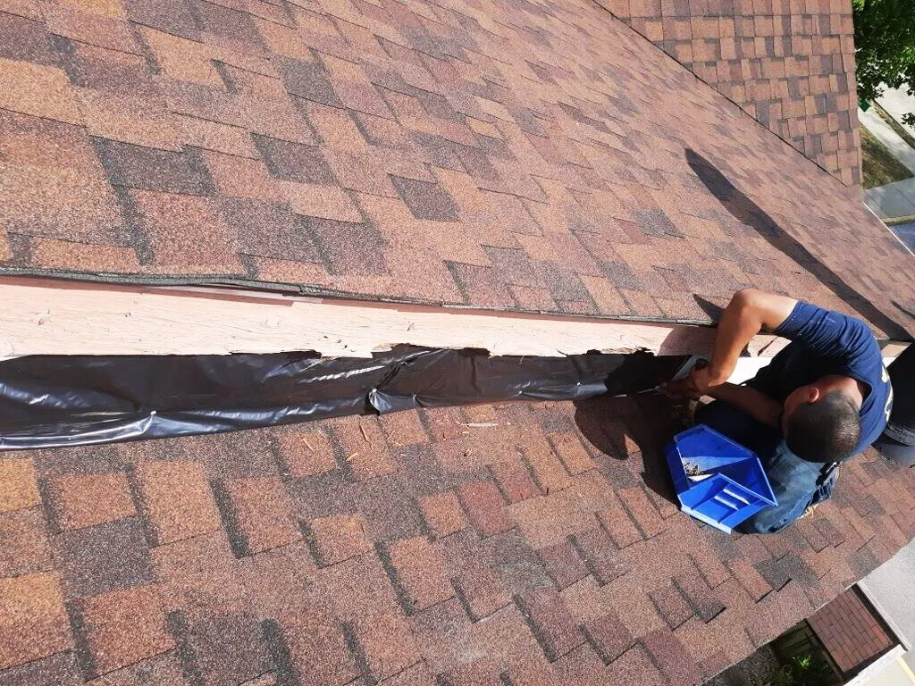 A contractor secures protective material along the roof ridge during a repair or installation. 🏠🔧