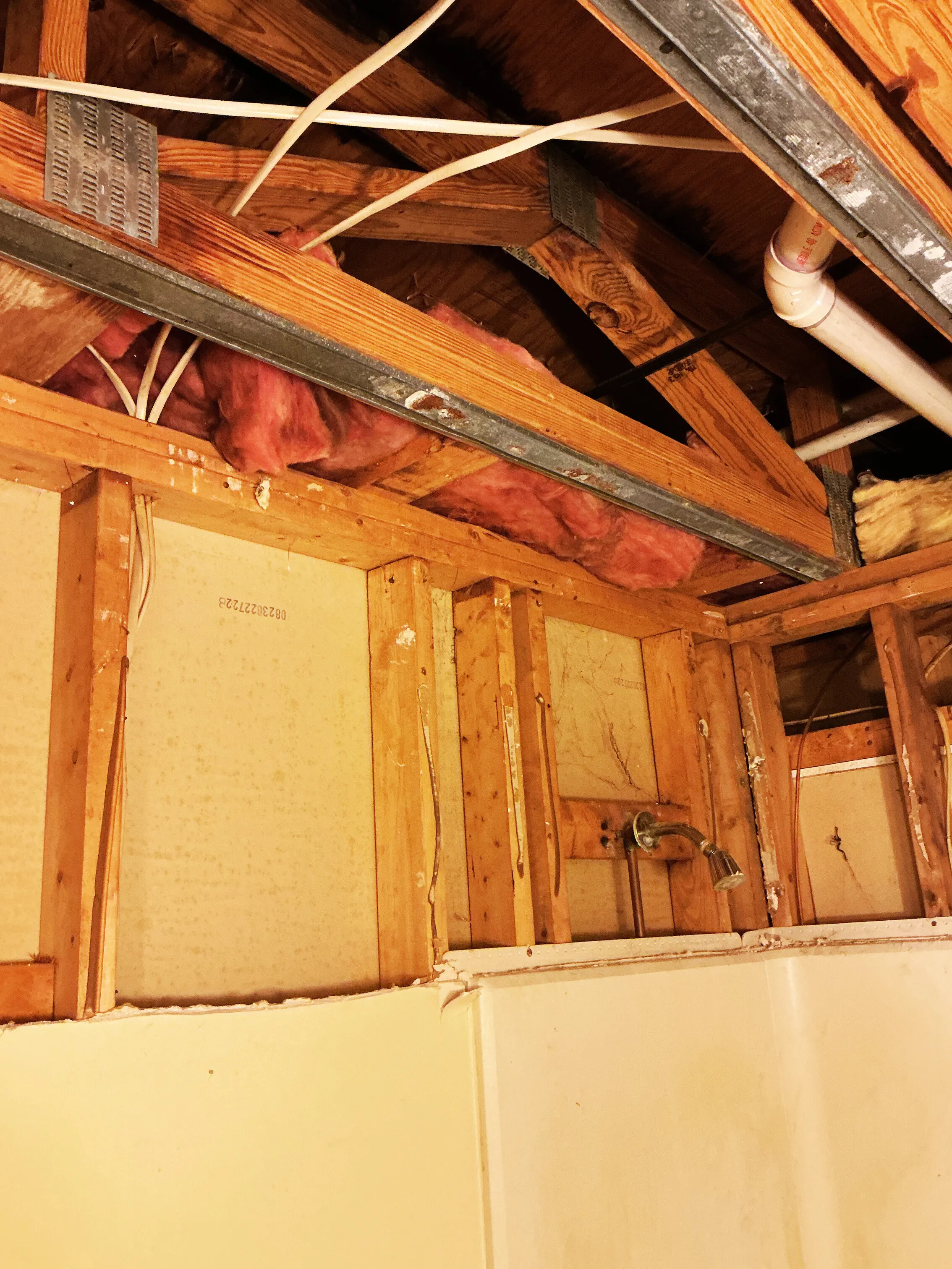 Bathroom wall opened during renovation, exposing wood framing, plumbing, and insulation above the shower. 🚿🔧